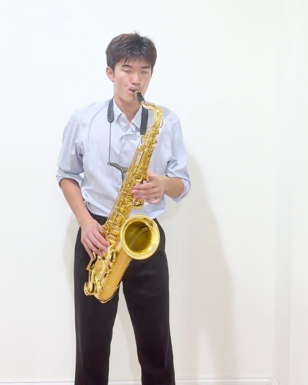 Ethan playing tenor saxophone against a white wall